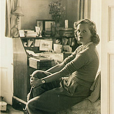 Daphne seating on the arm of a chair at her desk