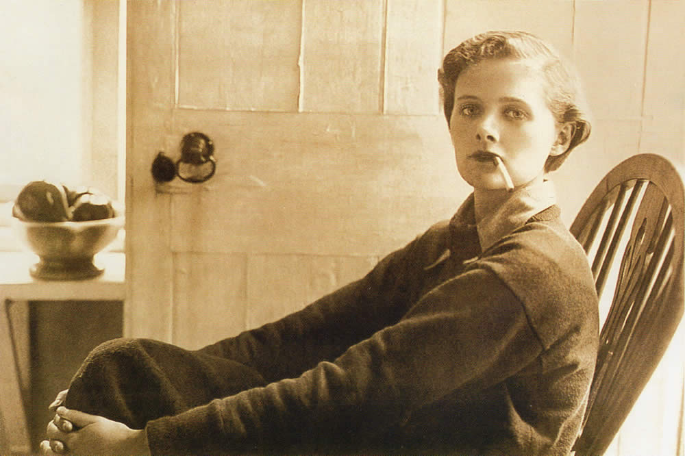 Daphne du Maurier, seated in a wooden chair smoking a cigarette, Ferryside November 1930