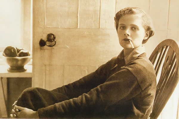 Daphne du Maurier, seated in a wooden chair smoking a cigarette, Ferryside November 1930